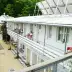 White building with balcony and red chairs, surrounded by greenery and a solar panel on the roof.