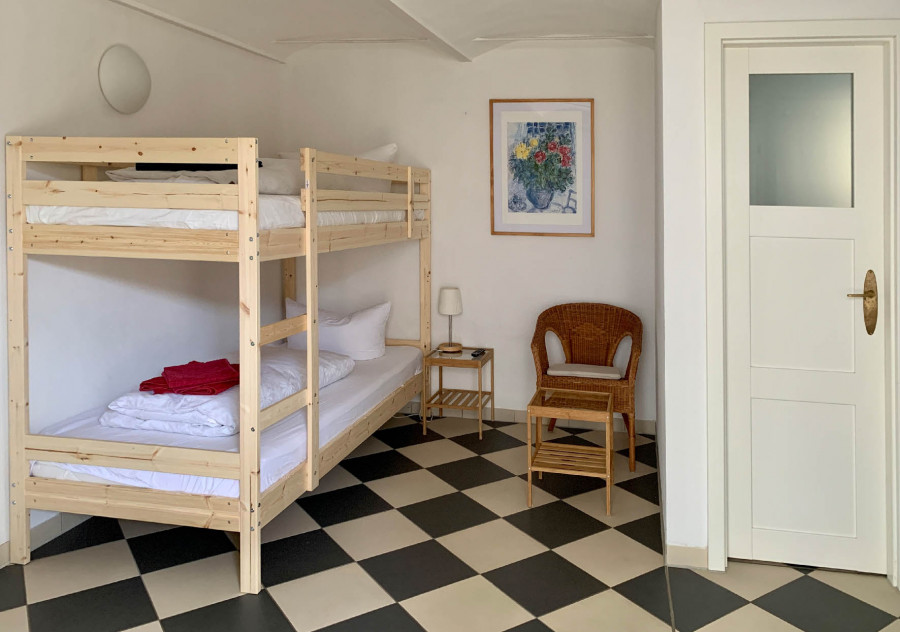 Room with two wooden bunk beds, black-and-white tiled floor, wicker chair, floral wall art, and a white door.