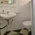 Small, clean bathroom with white tiled walls, sink, toilet, hairdryer mounted on wall, and sign for disposal of pads and tampons.