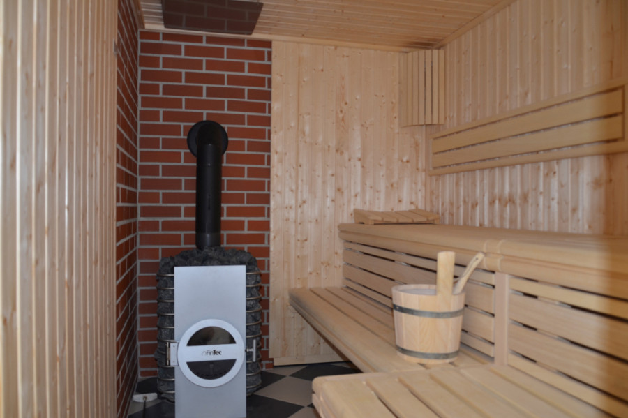 Wood sauna with fireplace, benches, bucket and wooden slats, warm ambiance, brick wall, FinTec heater