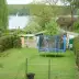 Green garden with trampoline, sheds and trees; sailboat on lake in background.