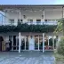 White two-story villa with balcony, ivy, and colorful prayer flags; outdoor area with tables, chairs, and Buddha statue on frost-covered terrace.