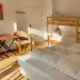 Small room with double bed, bunk bed, wooden table and chairs, colorful wall art in sunlight.