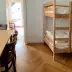 Wooden bunk bed with two mattresses, dining table and chairs in a bright room with parquet flooring and window opening.