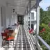 Long sunlit veranda with red chairs, black-and-white mosaic floor, and blooming roses along the railing, perfect for group trips or family gatherings.