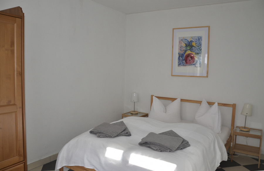 A minimalist bedroom with a wooden bed, two nightstands, a wardrobe, and an abstract painting on the wall.