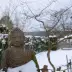 Estatua de Buda de piedra en la nieve, rodeada por &aacute;rboles desnudos y un paisaje de jard&iacute;n invernal.