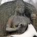 Estatua de piedra de una mujer con los ojos cerrados, sentada en un trono, parcialmente cubierta de nieve, en invierno.