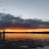 Atardecer sobre un lago con muelle, nubes anaranjadas y rojas en el horizonte y agua reflectante.